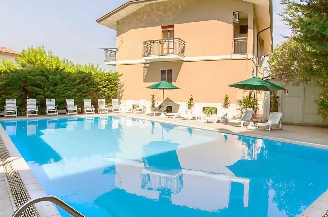 Piscina all'aperto con lettini e ombrelloni vicino a un edificio.