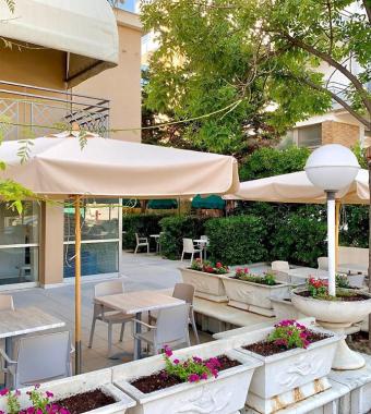 Terrazza esterna con tavoli, sedie, ombrelloni e piante in vaso.