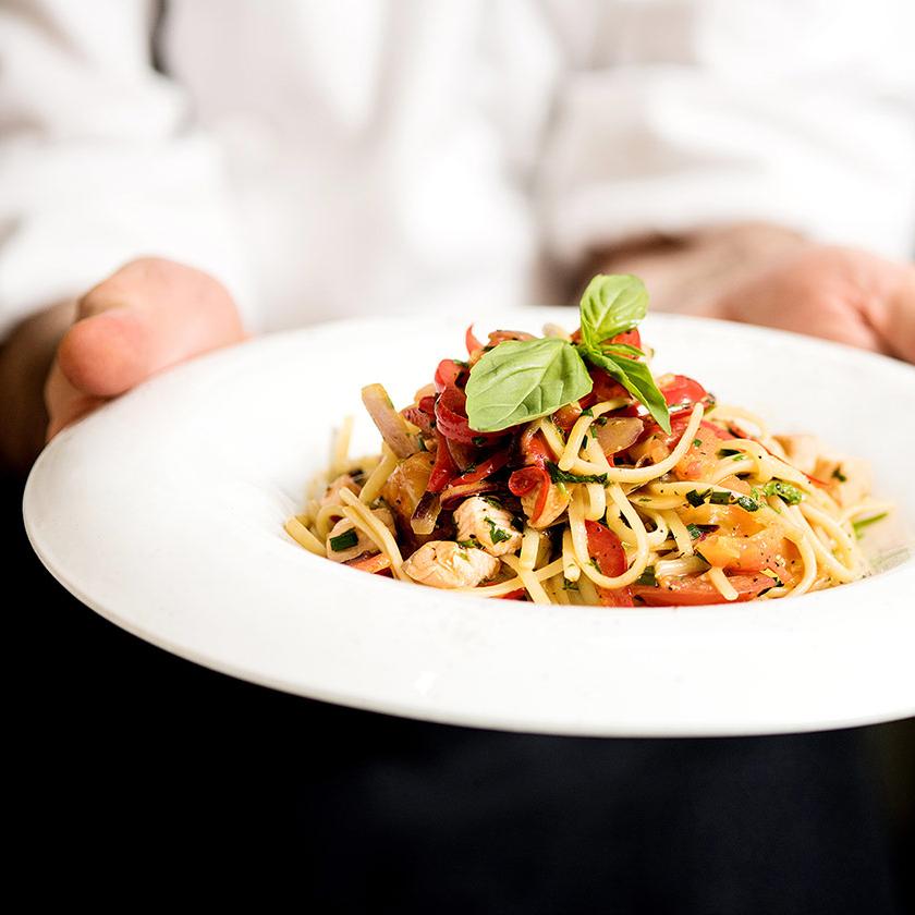 Piatto di spaghetti con pomodori, basilico e ingredienti freschi, servito da uno chef.