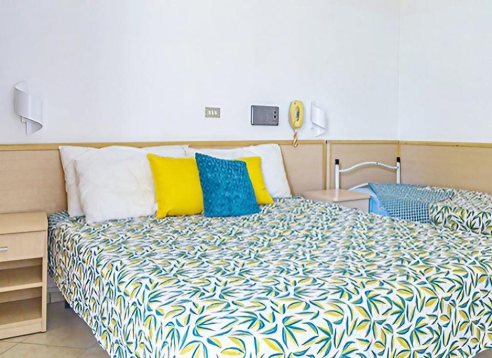 Camera da letto con letto matrimoniale, cuscini colorati e copriletto a fantasia.