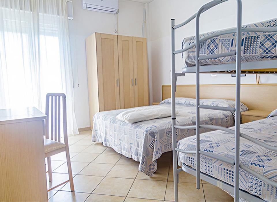 Camera luminosa con letto matrimoniale, letti a castello e arredamento semplice.